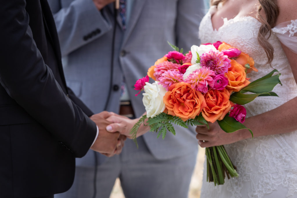 Close-up of bride and groom holding hands, and bride holding bouquet