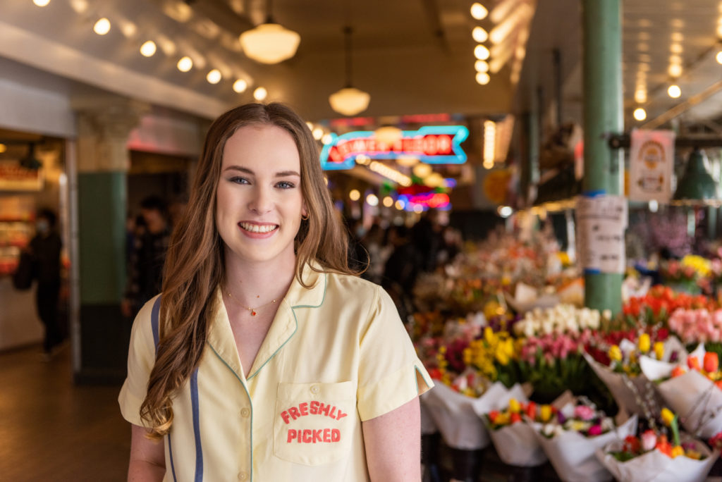 high school senior standing near flower stalls at Pike Place Market in Seattle