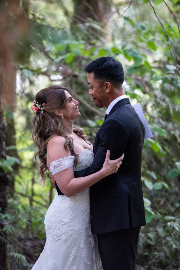 Bride and groom embracing in alcove surrounded by tall trees