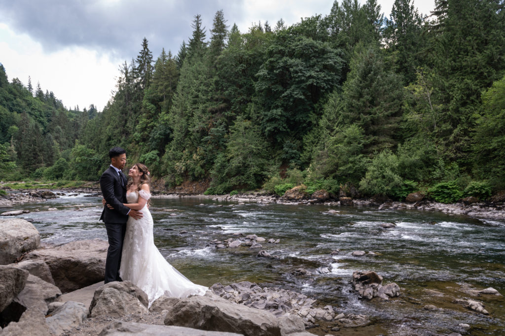 Bride and groom embracing while standing on large rocks along Snoqualmie River