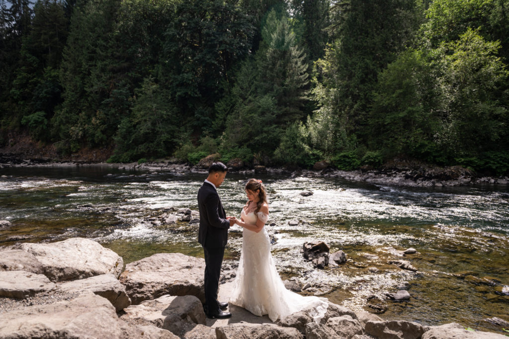 Bride and groom holding hands while standing on large rocks along Snoqualmie River