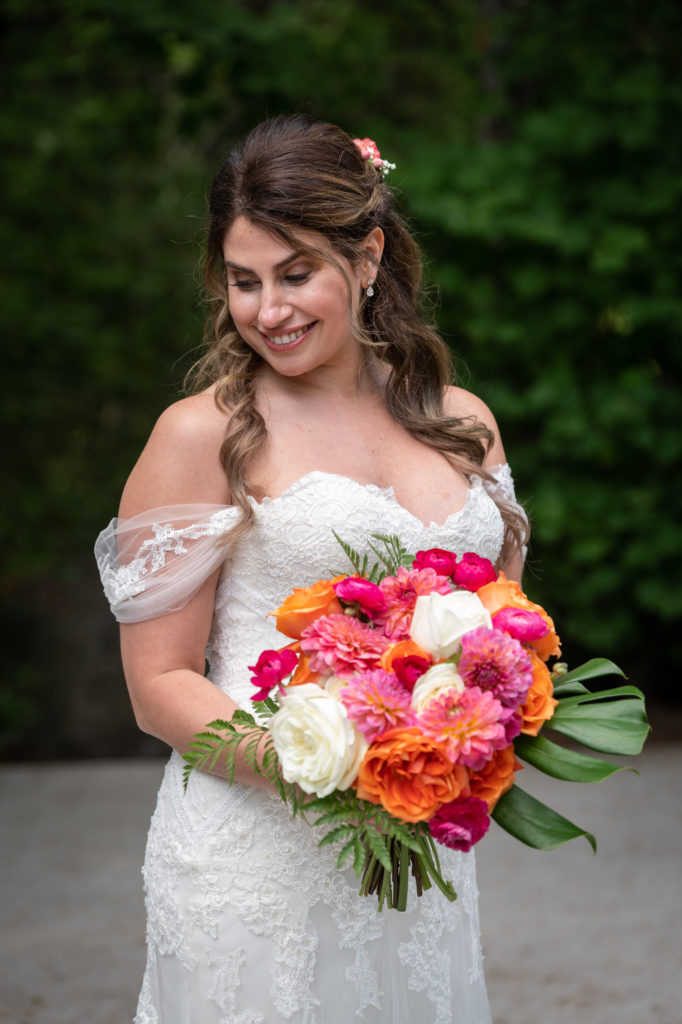Bride gazing down while holding orange, pink and white bouquet