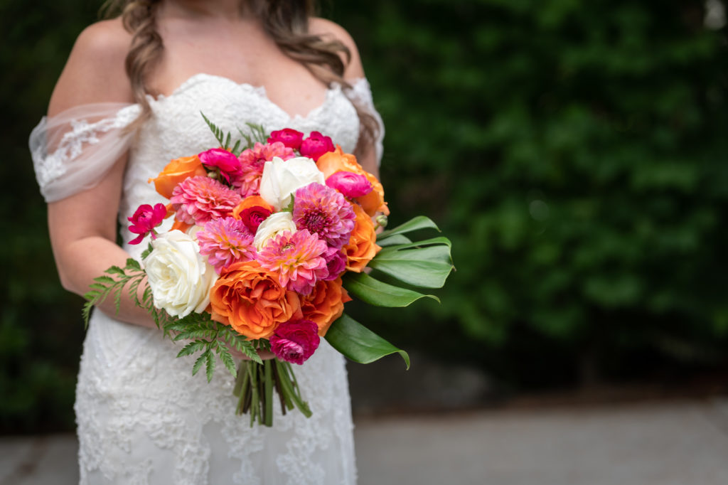 Close-up of bride holding orange, pink and white bouquet