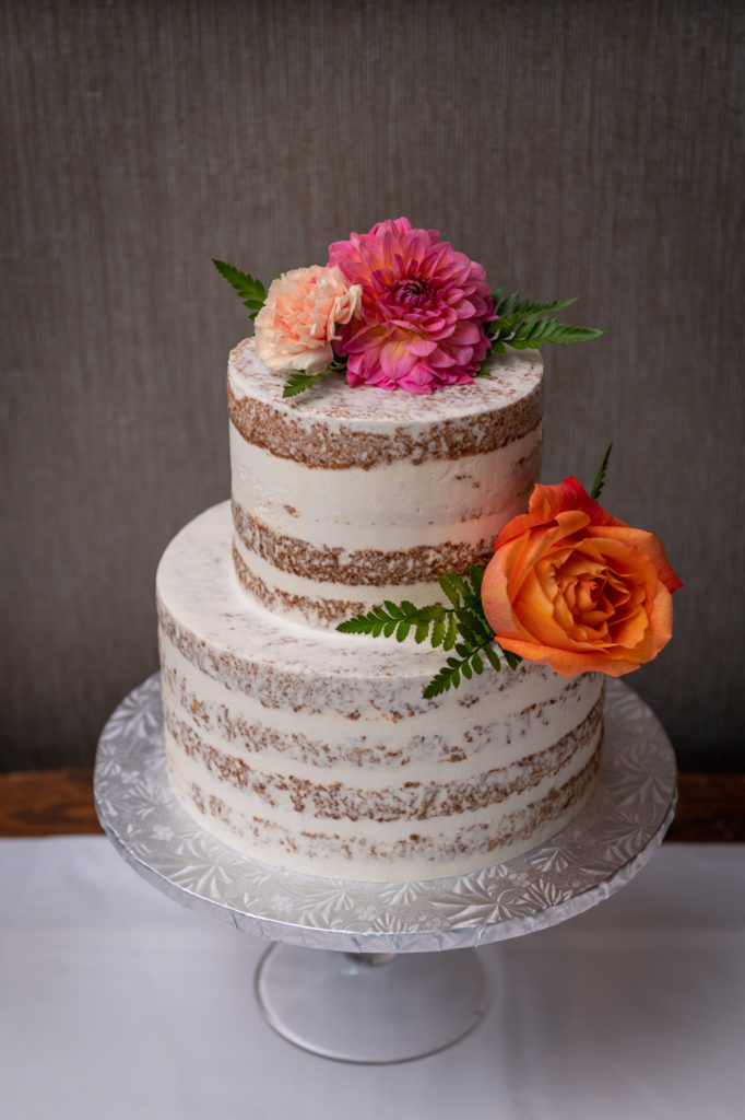 Naked wedding cake with white frosting and pink and orange floral decor