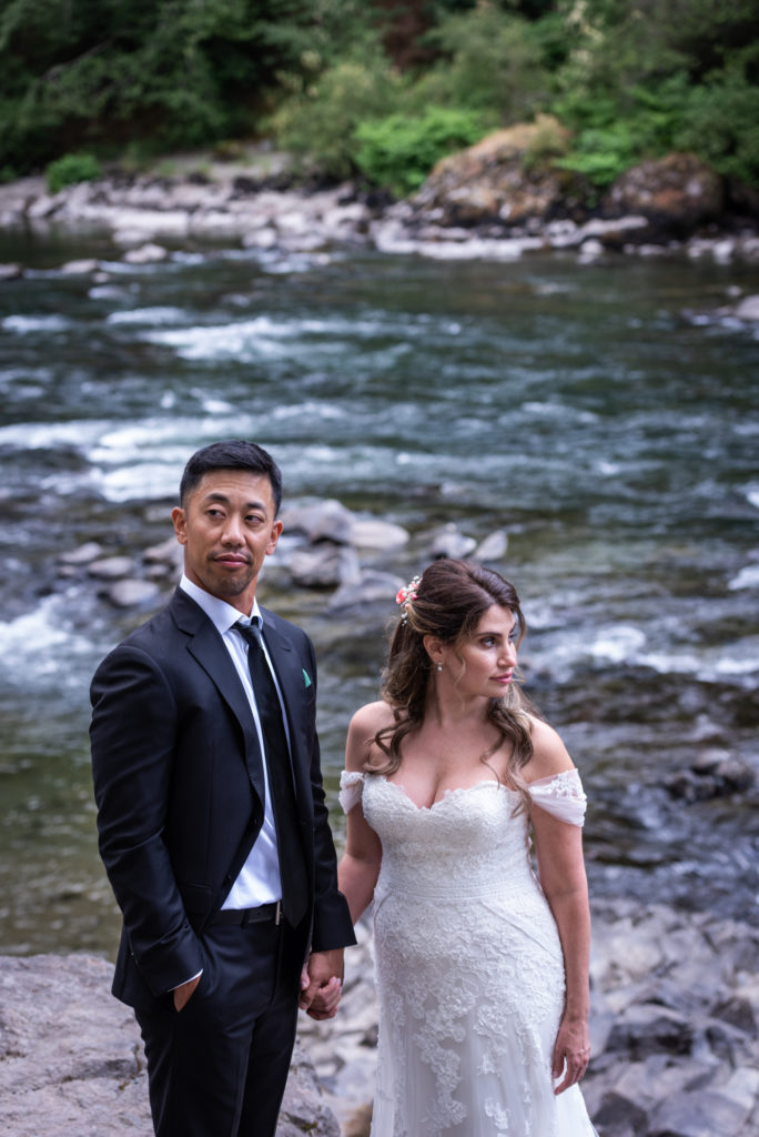 Bride and groom holding hands and looking in opposite directions with Snoqualmie River in background