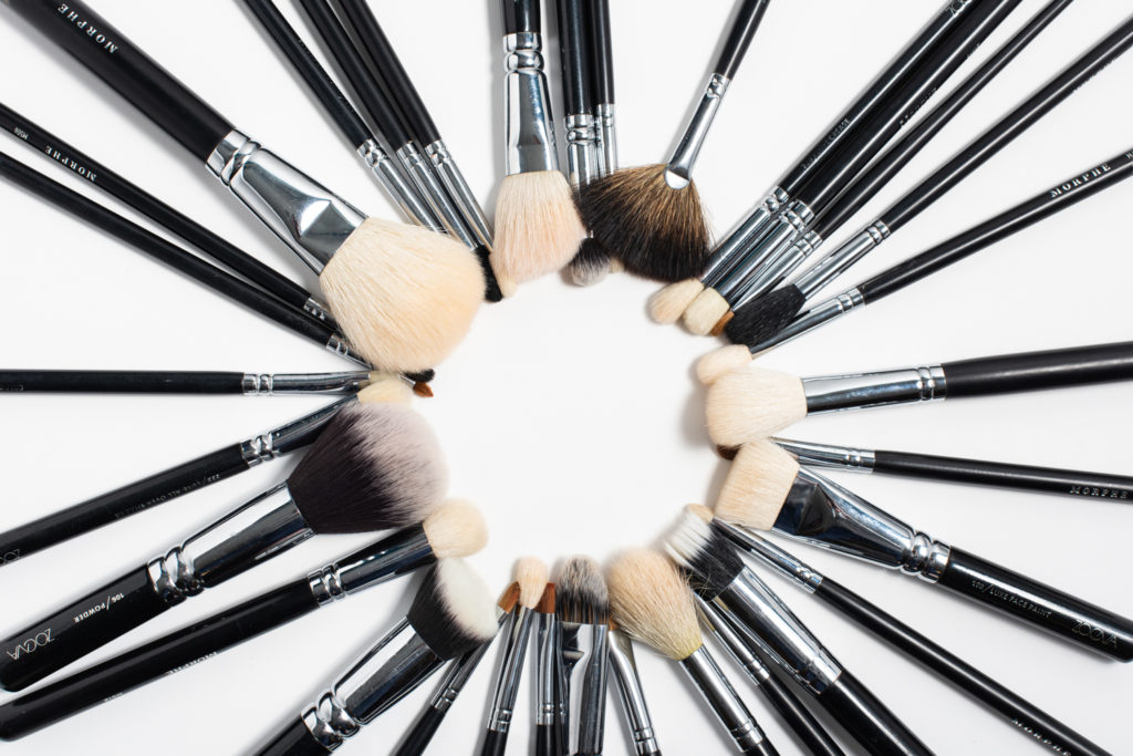 Black makeup brushes fanned in a circle on white backdrop