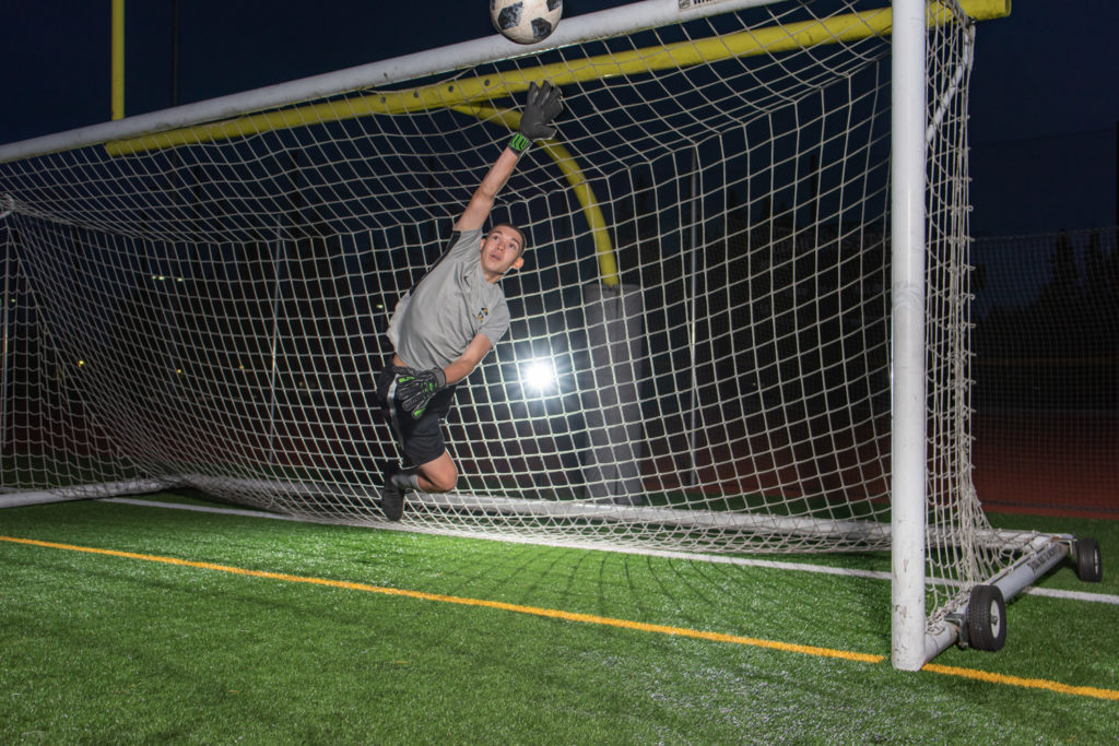 High school senior soccer goalie deflecting a soccer ball in the goal