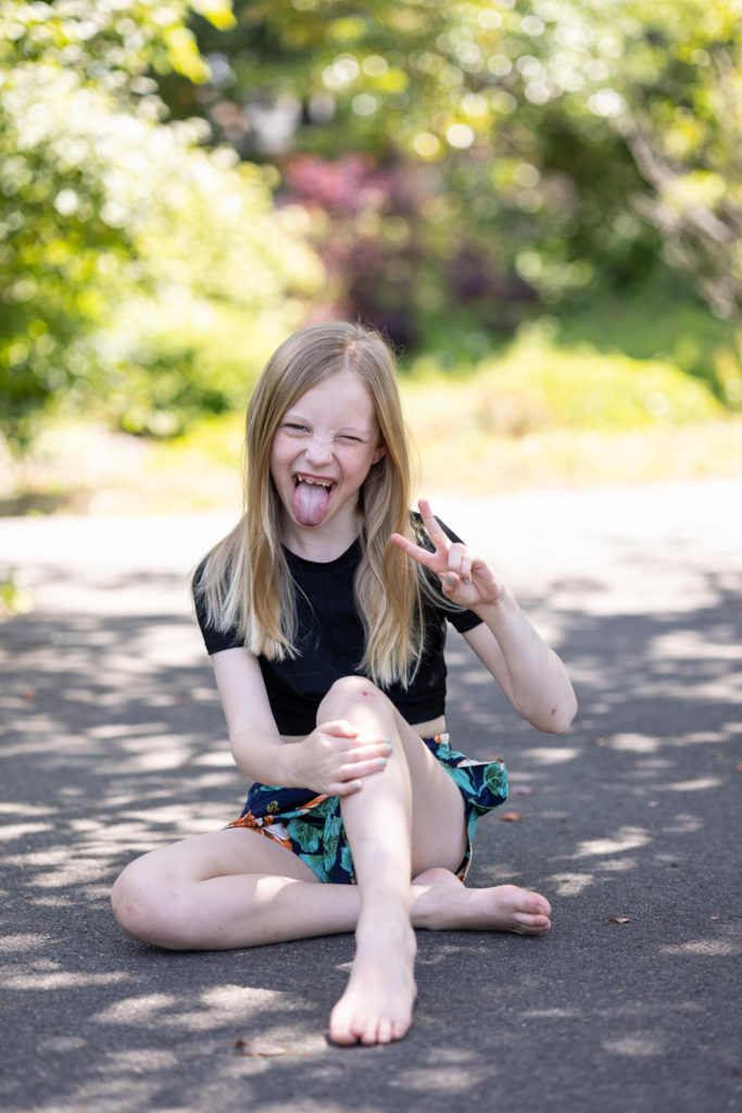 young girl sitting on ground sticking tongue out and making peace sign