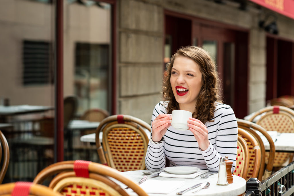young woman in a striped shirt holding a coffee cup at an outdoor cafe