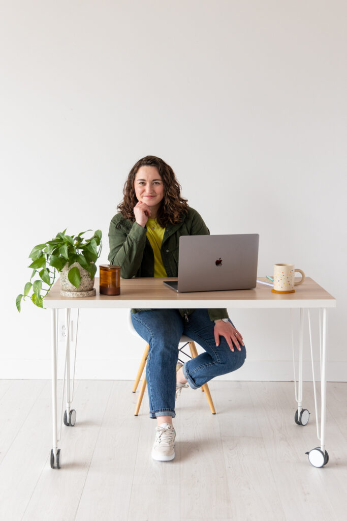 Woman sitting at desk with a plant, candle, laptop and mug on the desk.
