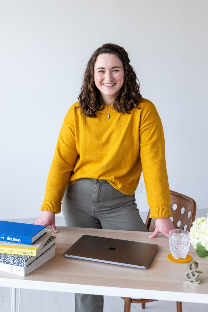 Woman standing behind a desk with books and laptop on the desk.
